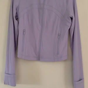 Ljuslila jacka från Lululemon - Snygg ljuslila jacka från Lululemon med dragkedja framtill och två fickor med dragkedja. Jackan är figursydd och har långa ärmar med tumhål. Tillverkad i en mix av nylon och elastan. Storlek 8 (40) men skulle mer säga 38. Aldrig använd💕slutsåld på hemsidan 