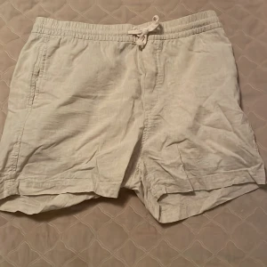 Beiga linneshorts från H&M med snörning - Säljer ett par beiga shorts från H&M i regular fit. De är gjorda i linne och har elastisk midja med snörning för skön passform. Perfekta för varma sommardagar och har en enkel, stilren look.