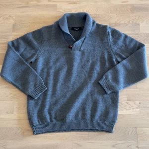 Grå stickad tröja från Zara Man - Säljer en grå stickad tröja från Zara Man i storlek L. Tröjan har en bred krage med knappdetalj och långa ärmar. Perfekt för kyliga dagar och enkel att matcha med jeans eller chinos.