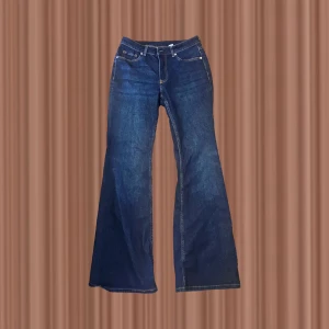 Blå bootcut jeans från H&M Divided - Snygga mörkblå bootcut jeans från H&M Divided med klassisk femficksdesign och kontrastsömmar. Jeansen har normal midja och är tillverkade i ett robust denimtyg som ger en cool och tidlös look. Perfekta för dig som gillar retrovibbar och vill sticka ut.