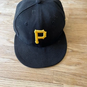 Svart New era keps - Svart keps med gul broderad P framtill, klassisk modell från Pittsburgh Pirates. Kepsen har böjd skärm och MLB-logga baktill. Tillverkad i bomull, perfekt för dig som gillar sportig streetstyle.