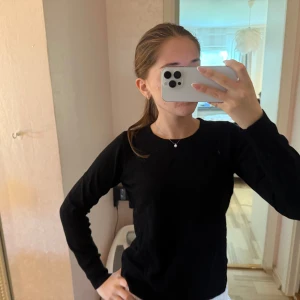 Svart långärmad stickad tröja - Enkel och stilren svart stickad tröja med rund halsringning och långa ärmar. Perfekt att matcha med jeans eller kjol för en clean look. Skön och mjuk känsla, passar till många tillfällen.