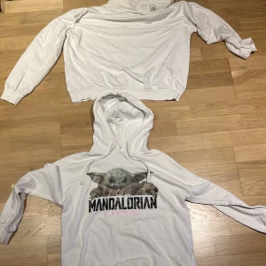 Vit Mandalorian hoodie med Baby Yoda - Säljer en vit hoodie med tryck av Baby Yoda och texten 'The Mandalorian' på bröstet. Tröjan har huva med snörning och långa ärmar. Perfekt för dig som älskar Star Wars och vill ha en chill och snygg look.