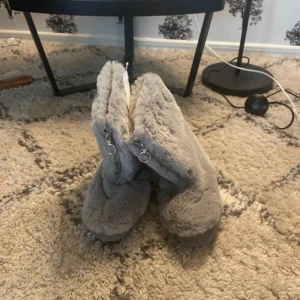 Grå fluffiga boots med dragkedja - Supermysiga grå boots i fluffigt syntetmaterial med dragkedja och rund tå. Perfekta för kalla dagar när du vill hålla fötterna varma och sköna. Snygg, chunky sula och coola ringdetaljer på dragkedjan. Stl 39.