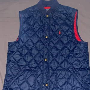 Marinblå Polo Ralph Lauren (väst) - Snygg quiltad dunväst från Polo Ralph Lauren i marinblått med röda detaljer och guldiga knappar. Nästan aldrig använd köpte för 1200 för några månader sedan och bara legat i garderoben. Pris kan diskuteras