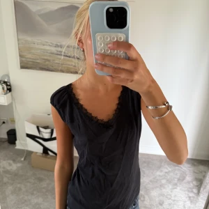 Svart ärmlös topp med spetskant - Svart ärmlös topp med v-ringning och fin spetskant runt halsen. Snygg och enkel modell som passar till jeans eller kjol. Stoleken är 38 men skulle säga att det är än S mer.
