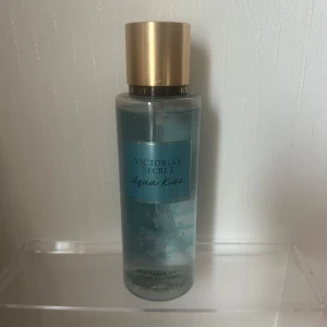 Victoria's Secret Aqua Kiss mist - Fräsch body mist från Victoria's Secret i doften Aqua Kiss. Flaskan är genomskinlig med blått innehåll och har ett stilrent guldigt lock. Rymmer 250 ml och har en modern, enkel design som känns lyxig och fräsch.