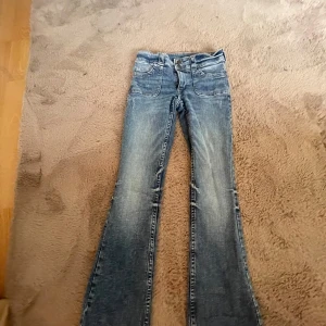 Blå bootcut jeans med dubbla knappar - Snygga blå jeans med bootcut-modell och dubbla knappar i midjan. Jeansen har klassiska fickor fram och bak, samt coola detaljer med knappar på bakfickorna. Säljer dom så dom har blivit för små i midjan 😊