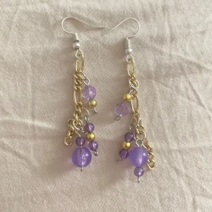 Lila pärlörhängen med kedjor - Snygga örhängen med guld- och silverfärgade kedjor och lila pärlor i olika storlekar. Några av pärlorna är facetterade för extra bling och det finns små guldfärgade detaljer. Perfekta för dig som vill sticka ut med färg och cool design.