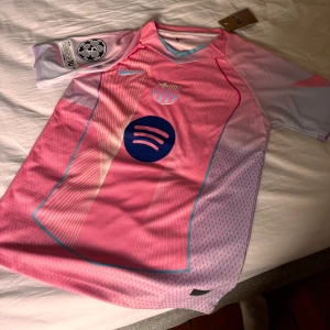 Rosa FC Barcelona Nike fotbollströja - Snygg FC Barcelona fotbollströja från Nike i en ljusrosa ton med vita och blå detaljer. Helt ny aldirg använd. 