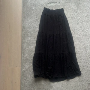 Svart långkjol från lager 157, storlek XS - Svart långkjol från lager 157t i storlek XS. Kjolen har en smockad midja som ger en skön och flexibel passform. Den är voluminös med flera lager och har en mjuk, flowy känsla. Perfekt för dig som gillar en enkel men snygg look.