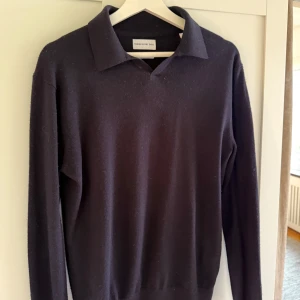 Svart merionoulls polotröja These Glory Days - Snygg svart merinoulls stickad polotröja från These Glory Days. Tröjan har klassisk krage, lång ärm och ribbade muddar. Perfekt till lager-på-lager och funkar året runt. 