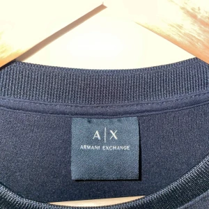 Svart långärmad tröja Armani Exchange - Svart långärmad tröja från Armani Exchange med rund hals och diskret svart logga tryckt framtill. Stilren och enkel design som passar perfekt till jeans eller chinos. Mjuk och bekväm bomullskvalitet.