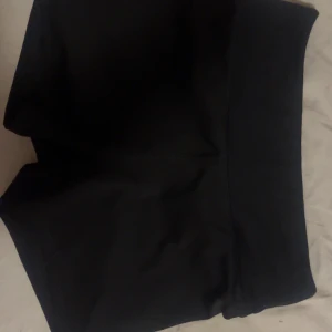 Svarta träningsshorts från H&M Move - Svarta, tighta träningsshorts från H&M Move med hög midja och slät design. Perfekta för gymmet eller sport, tillverkade i stretchigt syntetmaterial som sitter skönt och följer kroppen. Diskret logga framtill i samma färg som shortsen.