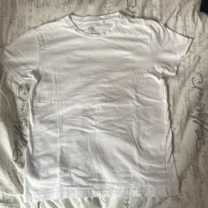 Vit basic t-shirt från 157 XS - En klassisk vit t-shirt från 157 i storlek XS. Modellen är enkel med rund hals och korta ärmar, tillverkad i mjuk 100% bomull. Perfekt för att bygga lager eller köra en clean look. Snygg att matcha med jeans eller shorts. Andvänd bara 1 gång.