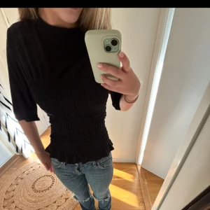 Svart smockad topp med volangkant - Svart topp med smockad midja och volangkant nertill. Endast använd 2 gånger😊