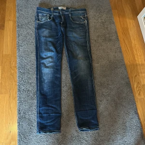 Replay blå jeans, rak modell - Snygga blå jeans från Replay med anbass modell och coola slitningar vid fickorna. Jeansen har 4 fickor, dragkedja och knapp i midjan. Materialet är slitstarkt denim och färgen är mörkblå med ljusare tvättade detaljer. Perfekt för dig som gillar en tidlös jeanslook. Och en uppklädd look 