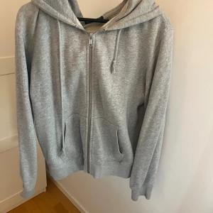 Grå hoodie från Brandy Melville - Grå zip-hoodie från Brandy Melville med huva och dragsko. Mjuk bomullsmix, två fickor framtill och långa ärmar. 