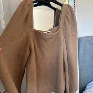 Beige stickad tröja med puffärm - Superfin beige stickad tröja med fyrkantig ringning och puffiga långärmar. Tröjan har en mjuk känsla och ribbade muddar nedtill. Perfekt för dig som gillar en stilren men ändå trendig look.