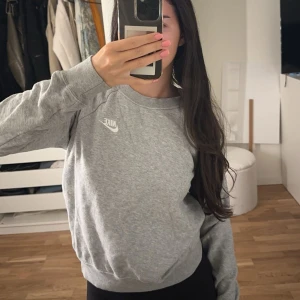 Grå sweatshirt från Nike XS - Säljer en klassisk grå sweatshirt från Nike i storlek XS. Tröjan har rund halsringning, långa ärmar och en vit Nike-logga på bröstet. Perfekt för en chill och sportig stil. Materialet är mjukt och skönt, troligtvis bomullsmix.