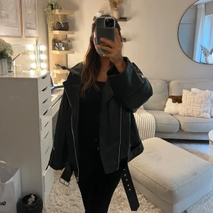 Svart oversized skinnjacka NA-KD - Säljer en svart oversized skinnjacka från NA-KD med coola dragkedjor, bred krage och bälte i midjan. Jackan har quiltat foder och långa ärmar. Endast använd vid ett tillfälle❤️