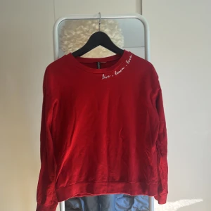 Röd sweatshirt med broderad text - Röd sweatshirt från H&M med vit broderad text 'live, learn, love' vid halsringningen. Tröjan har rund hals, långa ärmar och är gjord i mjuk bomull. Perfekt för en chill och avslappnad stil.