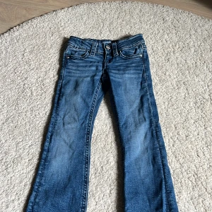 Blå bootcut jeans Gina Tricot 134 - Snygga blå jeans från Gina Tricot i storlek 134. Modellen har bootcut-ben, klassiska fickor fram och bak med dekorativa sömmar och knappar. Jeansen har en cool tvättad look och är tillverkade i mjukt denimtyg.