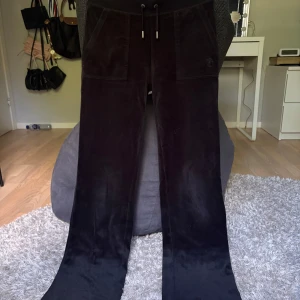 Svarta juicy couture byxor - Svarta velourbyxor från Juicy Couture i storlek XS. Byxorna har snörning i midjan och stora fickor fram samt bakfickor med silverknappar. Supermjuk känsla och klassisk Juicy-stil.Säljer matchande tröja!! Dem har blivit lite noppriga längs midjan och snörena, men det är inget man tänker på!!! Kontakta mig om du har några funderingar!!❤️
