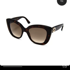 Gucci solglasögon Cat eye GG0327S 002 52 - Snygga Gucci solglasögon med breda bågar i brunmelerad mönster och klassisk cat-eye form modell:  GG0327S 002 52. Glasen är tonade och bågarna har en guldig Gucci-logga på sidorna. Kommer med originalfodrasosamt kvitto kan ordnas digitalt då dem.köptes online. Perfekt för dig som vill ha en lyxig och trendig look. Endast testade och säljer då det ej kommer till användning. Nypris mellan 2100-2800kr