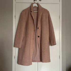 Rosa kappa från Zara Trafaluc - Säljer en superfin rosa kappa från Zara Trafaluc. Den har en mjuk, strukturerad yta, klassisk krage och knäpps med två knappar framtill. Fodrad insida och två fickor på sidorna. Perfekt för dig som vill ha en stilren och mysig look.