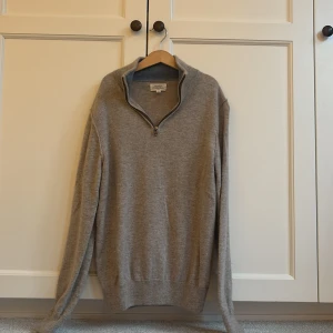 Grå halvzip-tröja från Hartford - Säljer en stilren grå långärmad tröja från Hartford med halv dragkedja i halsen. Tröjan är i mjukt material och har ribbade muddar samt krage. Perfekt för lager-på-lager och chill dagar.