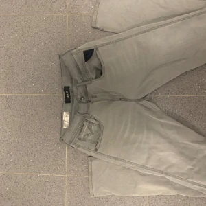 Replay Anbass ljusgrå jeans, stl 30 - Säljer ett par snygga Replay Anbass jeans i ljusgrå färg. Modellen har klassisk femficksdesign, och diskreta detaljer på bakfickorna. Jeansen är tillverkade i mjuk bomullsdenim med lite stretch för extra komfort.