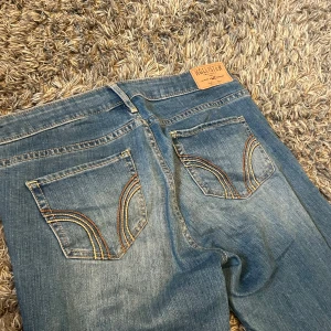 Blå jeans från Hollister med broderade fickor - Säljer ett par blå jeans från Hollister med snygga broderade detaljer på bakfickorna. Jeansen är straight och lågmidjade