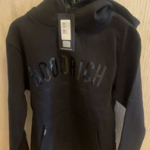 Svart hoodie från Hoodrich, storlek S - Säljer en svart hoodie från Hoodrich med stor logga framtill och texten 'From Nothing To Something'. Tröjan har huva, magficka och är i mjukt material. Perfekt för dig som gillar streetwear och vill ha en stilren look. Helt ny 