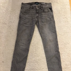 Replay Anbass grå jeans slim fit - Grå jeans från Replay, modell Anbass, med ett håll i ena bakficka och klassiska fem fickor. Slim fit passform och raka ben, tillverkade i mjukt jeanstyg. Coola broderade bakfickor och diskret Replay-märke. Perfekt för dig som gillar streetstyle.