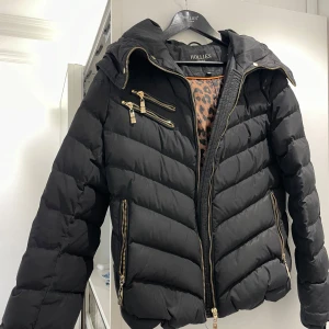 Svart pufferjacka från Hollies 350kr   Med päls 450 - Säljer en svart pufferjacka från Hollies med guldfärgade dragkedjor och avtagbar huva. Jackan har leopardmönstrat innerfoder och medföljer en fuskpäls att fästa på huvan. Perfekt för kalla dagar och riktigt snygg detalj med gulddragkedjor.