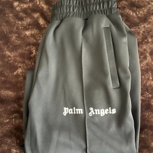 Svarta Palm Angels mjukisbyxor - Svarta mjukisbyxor från Palm Angels med vit logga på framsidan och vita ränder längs sidorna. Byxorna har elastisk midja med dragsko och raka ben. Tillverkade i polyester för en sportig vibe och skön passform.