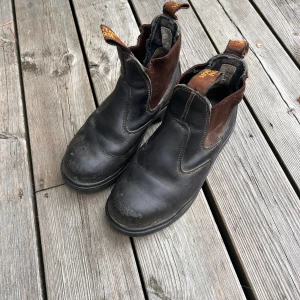 Mörkbruna Mountain Horse med stålhätta - Klassiska jodhpurs i mörkbrunt skinn med elastiska paneler på sidorna. Stålhätta för säker vistelse i stallet. Grov sula för extra grepp och dragflikar med logga både fram och bak. Storlek 36