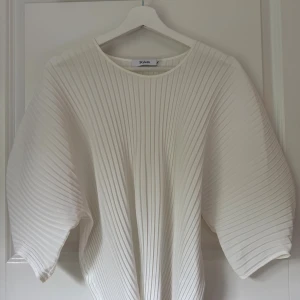 Vit plisserad blus från Stylein - Säljer en superfin vit plisserad blus från Stylein i nyskick. Blusen har vida trekvartsärmar och en rund halsringning. Materialet är lätt och ger ett snyggt fall. Perfekt för dig som gillar stilrena och trendiga plagg.