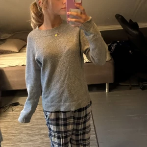 Grå stickad tröja - Mysig grå stickad tröja med rund halsringning och ribbade muddar vid ärmslut och nederkant. Perfekt för kyliga dagar och enkel att matcha med olika outfits. Klassisk och stilren modell som passar till det mesta.