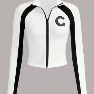 Vit och svart croppad ziptröja - Snygg croppad tröja i vitt med svarta ränder längs ärmarna och dragkedja framtill. Tröjan har ett stort C på bröstet och lång ärm. Perfekt för en sportig och trendig look.