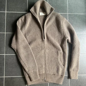 Beige stickad kofta från Zara  - Ribbstickad beige kofta från Zara Origins med hög krage och hel dragkedja framtill. Tröjan har långa ärmar, två fickor och är gjord i ett mjukt stickat material. Perfekt för lager-på-lager och chillare dagar.