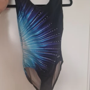 Blå och svart gymnastikdräkt från TreFit - Snygg gymnastikdräkt med coolt blått och svart mönster som strålar ut från mitten, dekorerad med små vita prickar. Materialet är mjukt och stretchigt syntet, Rund halsringning och klassisk passform.