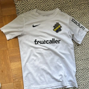 Vit AIK fotbollströja Nike XL - AIK:s officiella bortatröja i vitt från Nike, storlek XL. Tröjan har klubbmärke på bröstet, svart Nike-logga, sponsorer som Truecaller och Stadium samt nummer 10 och SVEA på ryggen. Tillverkad i Dri-FIT-material som andas.