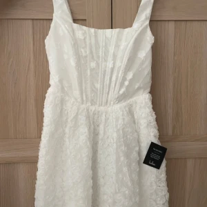 White mini dress - Felköpt, använt ej. Wrong order, not used. Bust: Great for any cup size. Waist: Fitted - elastic waist allows stretch. Hip: Not Fitted - fuller skirt allows room for hips. Undergarments: May be worn with a strapless bra, adhesive bra, petals, or no bra. Fabric: Fabric has no stretch. Length: Mid-thigh. Size M measures approximately 34.5" from shoulder to hem. Details Shell: 100% Polyester. Lining: 100% Polyester.
