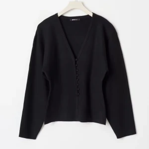 Svart kofta med v-ringning från Gina Tricot - Säljer en svart kofta från Gina Tricot med djup v-ringning och snygga knappar framtill. Koftan har långärmade, lite loose ärmar och är gjord i mjukt stickat material. Slutsåld❤️