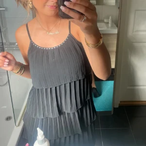 Volang klänning - Säljer en svart plisserad kortklänning med tunna axelband och pärldetaljer längs halsringningen. Klänningen har lager på lager-effekt med volanger och ger en riktigt snygg och ungdomlig vibe. Perfekt för dig som gillar stilrena och trendiga plagg. För liten för mig jag är 161!❤️