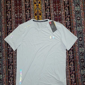 Vit Under Armour t-shirt HeatGear - Snygg vit t-shirt från Under Armour med reflekterande logga och detaljer. Modellen är kortärmad och har en rund hals. Materialet är lätt och andas, perfekt för träning. Diskret tryck på ärmen och nederkant, samt 'Threadborne' insida vid halsen.