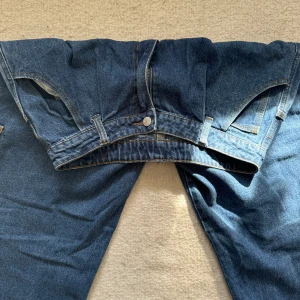 Wake Jeans mörkblå cargobyxor - Mörkblå cargobyxor från Wake Jeans med broderad logga på bakfickan. Byxorna har flera fickor, inklusive sidofickor med lock, och klassisk jeansknapp. Avslappnad passform och tillverkade i robust denim. Perfekta för en chill streetwear-look.