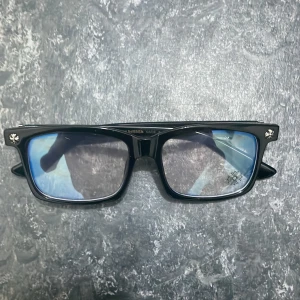 Svarta glasögon från Chrome Hearts - Säljer en svart jacka från Chrome Hearts med klassisk rak form och coola detaljer. Jackan har silverfärgade knappar och dragkedja, samt broderade blommor på axlarna och ärmarna. Materialet är slitstark bomull och polyester, perfekt för dig som gillar streetwear med lyxig vibe. INGEN BOX, Anti blue